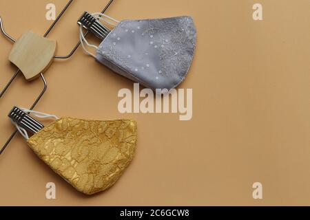 Maschere facciali riutilizzabili in pizzo d'oro e d'argento appese su appendiabiti. Maschera di tessuto da cucire per prevenire lo scoppio del virus Covid-19 e l'inquinamento da polvere . Foto Stock