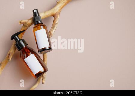 Cosmetici SPA branding mockup. Bottiglie in vetro ambrato scuro con etichette bianche per testo su ramo di legno. Flacone dispenser a pompa per spray per cosmetici e corpo b Foto Stock