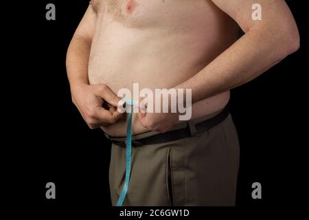 Uomo grasso tenendo un nastro di misurazione, misurare l'addome. Perdita di peso. Foto su sfondo nero isolata Foto Stock