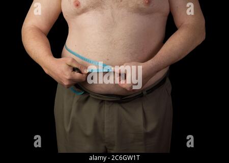 Uomo grasso tenendo un nastro di misurazione, misurare l'addome. Perdita di peso. Foto su sfondo nero isolata Foto Stock