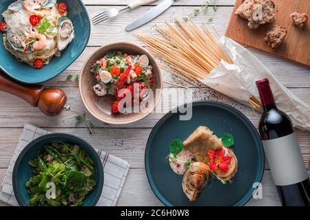 Spaghetti con gamberi su piastra di ceramica bianca e serviti con bottiglia di vino rosso. Vari ingredienti freschi sui lati. Vista dall'alto, disposizione piatta. Foto Stock