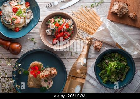 Spaghetti con gamberi su piastra di ceramica bianca e serviti con bottiglia di vino rosso. Vari ingredienti freschi sui lati. Vista dall'alto, disposizione piatta. Foto Stock