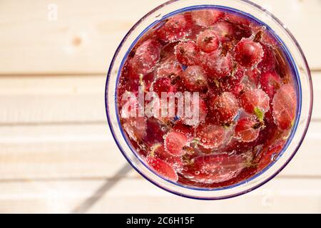 Bicchiere di rinfrescante drink estivo con frutti di bosco e cubetti di ghiaccio sul tavolo vicino.rinfrescante bevanda estiva con uva spina. Foto Stock