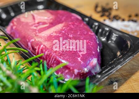 Bistecca di manzo in confezionamento sottovuoto e spezie su tagliere di legno Foto Stock