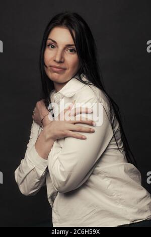 ritratto di una giovane donna su sfondo nero in abiti bianchi. Si copre con le mani. Foto Stock