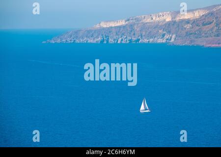 Costa rocciosa dell'isola greca in una giornata di sole. Yacht a vela bianco. Vista aerea Foto Stock