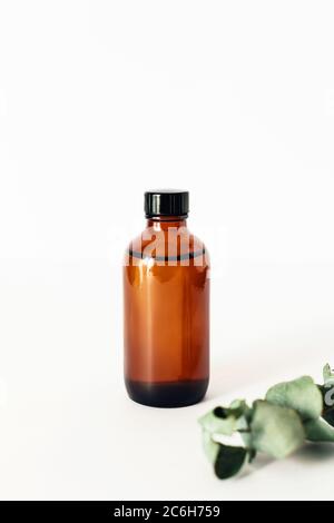 Una bottiglia di olio essenziale su sfondo bianco circondata da sprig di eucalipto. Foto Stock