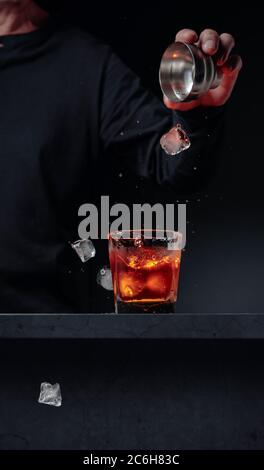 Il barista getta i cubetti di ghiaccio in un bicchiere al bar. Bevanda alcolica con spruzzi in un bicchiere smerigliato. Messa a fuoco selettiva, spazio di copia. Foto Stock