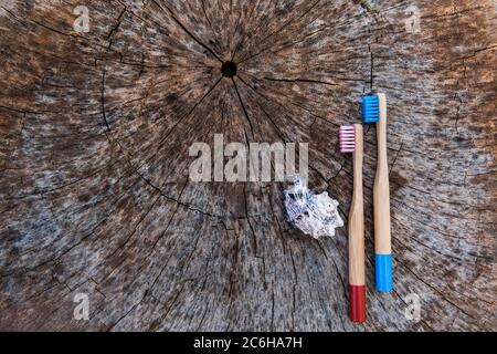 Due spazzolini da denti in legno di bambù ecologici rosa e blu su sfondo di legno con guscio. Spazio di copia, disposizione piatta. Foto Stock