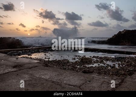 L'antico porto di Cesarea, Israele al tramonto. Le onde si stanno rompendo sulla frangiflutti Foto Stock