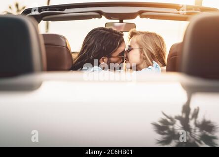 Felice coppia baciando in auto convertibile - persone romantiche che hanno momento tenero durante il viaggio su strada in città tropicale Foto Stock