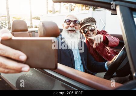 Felice coppia senior che prende selfie su nuova auto convertibile - persone mature divertirsi in cabriolet insieme durante la vacanza viaggio su strada Foto Stock