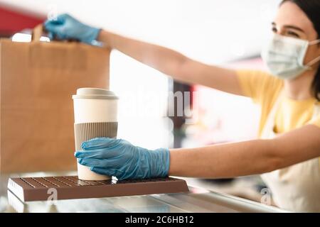 Il proprietario del bar lavora solo con gli ordini di take away durante l'epidemia di virus corona - giovane donna operatrice che indossa la maschera chirurgica del viso che dà pasto da asporto Foto Stock