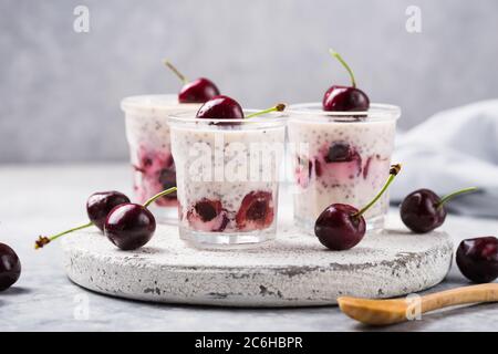 Budino di Chia con ciliegi, yogurt naturale, in un bicchiere su una superficie grigia. Messa a fuoco selettiva. Dessert sano, nutrizione adeguata, cibo super. Foto Stock