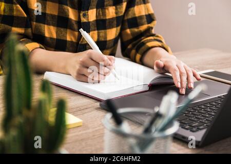 mettere in primo piano le mani di un lavoratore o di uno studente che fa avvisi con una penna bianca nel notebook mentre si naviga sul computer. lavorare e imparare da remoto Foto Stock