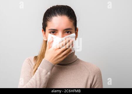 ritratto della giovane donna che copre le vie respiratorie con un tovagliolo di carta e guarda direttamente nella fotocamera su sfondo grigio Foto Stock