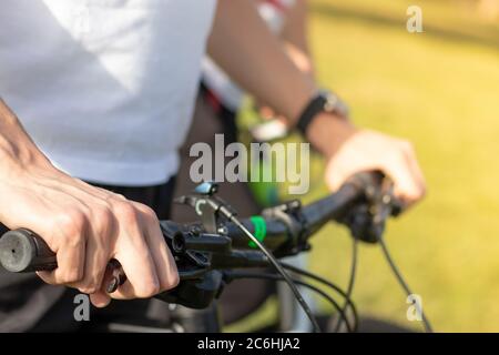 Primo piano di una mano mans che tiene il volante della bicicletta, tenendo premuto il freno. Vista a entrambe le mani, preparano per iniziare a fare il ciclismo all'aperto Foto Stock