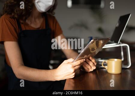 Sezione centrale della donna che indossa la maschera facciale utilizzando un tablet digitale a casa Foto Stock