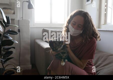 Donna che indossa maschera facciale che tiene il suo gatto a casa Foto Stock