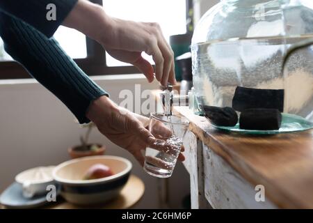 Sezione centrale di donna che versa l'acqua in un bicchiere a casa Foto Stock