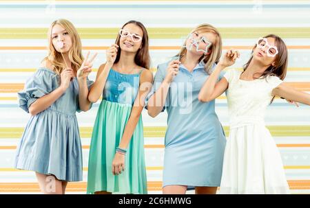 Ragazze adolescenti sorridenti graziose in abiti in piedi insieme con balloni alla festa di compleanno sullo sfondo colorato a righe Foto Stock