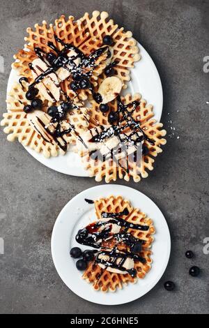 Wafer con cioccolato, banana e bacche su un piatto bianco. Foto Stock