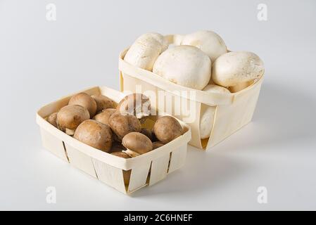 Camioncini bianchi e marroni di funghi in cesto di legno su sfondo chiaro. Primo piano. Champignon al cestino. Foto Stock