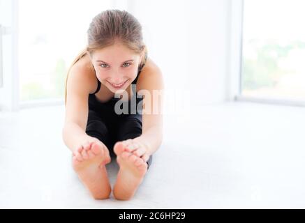 Ballerina giovane bella facendo stretching in stanza bianca Foto Stock