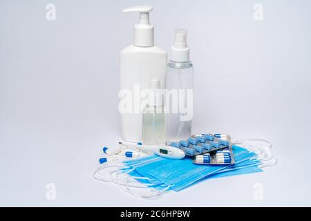 flacone di disinfettante o sapone liquido, maschera protettiva, blister di pillole medicinali e termometro su sfondo grigio chiaro Foto Stock