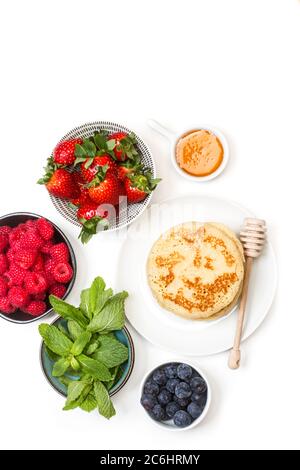 Pancake su un piatto e frutti di bosco in ciotole su sfondo bianco Foto Stock