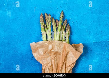 Asparagi verdi in un sacchetto di carta su uno sfondo blu testurizzato classico Foto Stock
