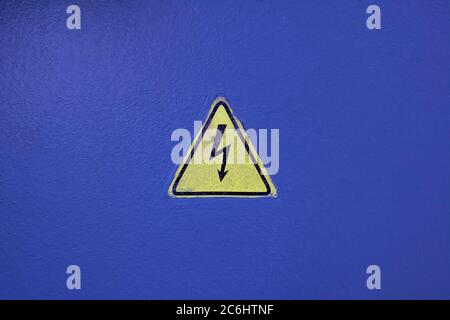 Cartello giallo sull'elettricità su una parete blu Foto Stock