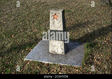 Monumento commemorativo e tomba di un soldato sovietico sconosciuto dell'esercito rosso. Lapide con stella rossa. Erba e foglie intorno luogo Foto Stock