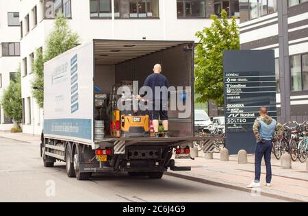 Consegna uomo dumper scaricato con un carrello elevatore a forche su un caricatore a portellone di un carrello di consegna di fronte a un edificio di uffici. Copenaghen, Danimarca - 10 luglio 20 Foto Stock