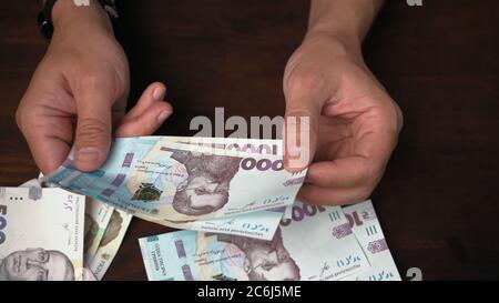 L'uomo considera i nuovi soldi di carta ucraini. Mani maschili che tengono il pacco di banconote valore nominale 1000, mille hryvnia su fondo di legno. Primo piano Foto Stock