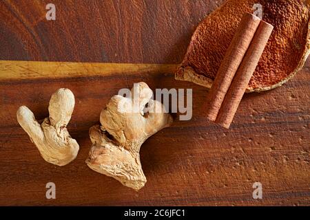Spezie secche di pacciamatura (zenzero, scorza d'arancia, bastone di cannella) su tavola di legno. Foto Stock