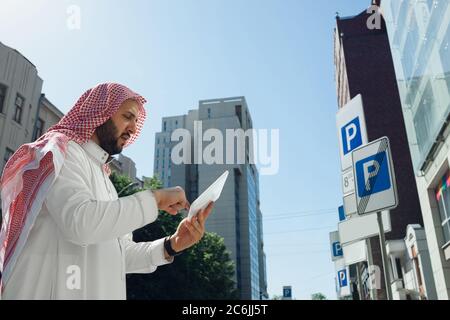 Ricco ritratto di uomo arabo durante l'acquisto di immobili, centro affari in città. Etnia, cultura, inclusione. Uomo d'affari sicuro in usura tradizionale che fa un affare riuscito. Finanza, economia. Foto Stock