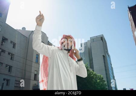 Ricco ritratto di uomo arabo durante l'acquisto di immobili, centro affari in città. Etnia, cultura, inclusione. Uomo d'affari sicuro in usura tradizionale che fa un affare riuscito. Finanza, economia. Foto Stock