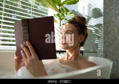 Donna che legge libro in una vasca da bagno Foto Stock
