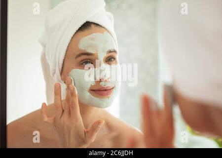 Donna che applica il pacchetto di faccia mentre osserva nello specchio Foto Stock