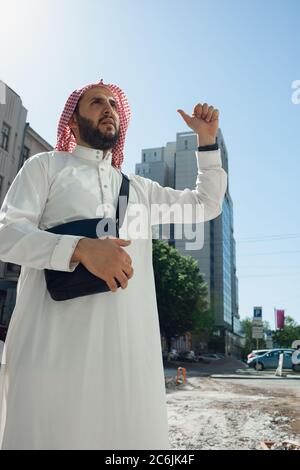 Ritratto ricco uomo arabo durante l'acquisto di immobili, casa vivente in città. Etnia, cultura, diversità. Uomo d'affari sicuro in usura tradizionale che fa un affare riuscito. Finanza, economia. Foto Stock