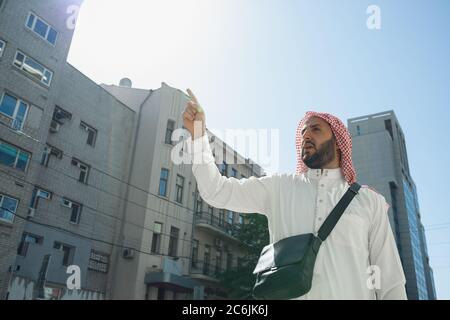 Ritratto ricco uomo arabo durante l'acquisto di immobili, casa vivente in città. Etnia, cultura, diversità. Uomo d'affari sicuro in usura tradizionale che fa un affare riuscito. Finanza, economia. Foto Stock