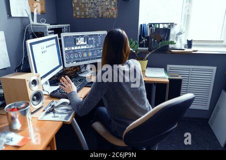 Femmina dai capelli scuri si siede al tavolo da ufficio circondato da Technics e Works in Video Editor. La ragazza è appassionata di lavorare al computer. Stock di Lipik Foto Stock