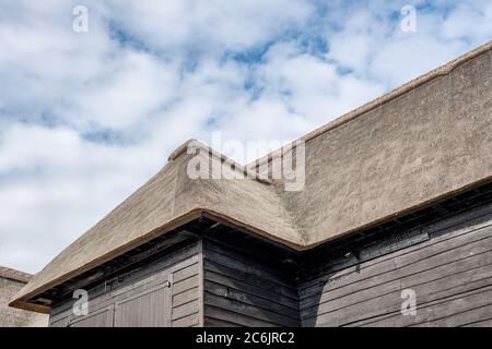 Aspetto esterno di un grande edificio agricolo e di stoccaggio costruito in legno, con il suo tetto rinnovato e con tetto in paglia. Le porte di ingresso sono chiuse. Foto Stock