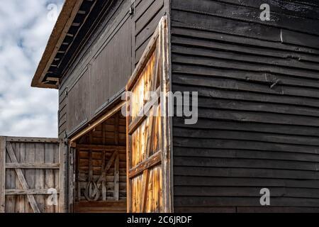 Aspetto esterno di un grande edificio agricolo e di stoccaggio costruito in legno, con il suo tetto rinnovato e con tetto in paglia. Le porte di ingresso sono chiuse. Foto Stock