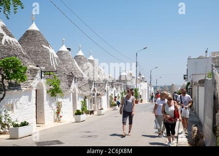 Puglia, Italia - Alberobello, turisti camminano per le strade della città pugliese con tetti a forma di cono costruiti in pietra, città dell'UNESCO. Foto Stock