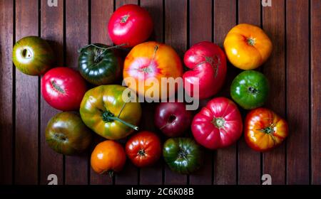 Varietà di pomodori rari multicolore. Colorati pomodori rossi, gialli, verdi, arancioni e neri su tavolo di legno marrone scuro, vista dall'alto Foto Stock