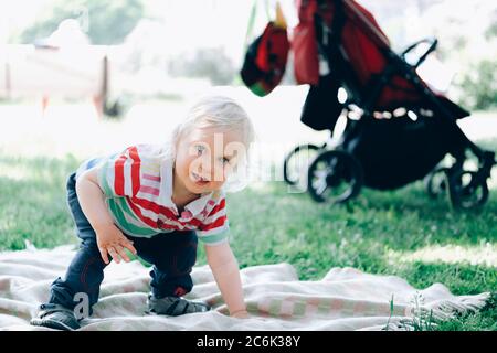 Ritratto di un ragazzo biondo che fa i primi passi, cercando di alzarsi in piedi in un parkin estivo una giornata di sole. Foto Stock