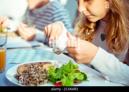 Primo piano foto delle mani della bambina che mangia una sana cena con insalata fresca, quinoa e pesce sulla terrazza Foto Stock