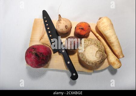 Verdure di radice diverse su tavola di taglio di legno insieme con coltello. Sfondo bianco. Vista ad angolo alto. Foto Stock